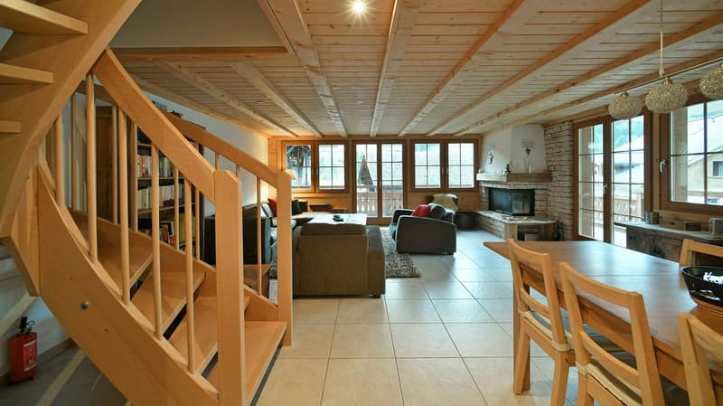 Open living space, fireplace, wooden dining table, bookshelves, couches, armchairs, wooden staircase