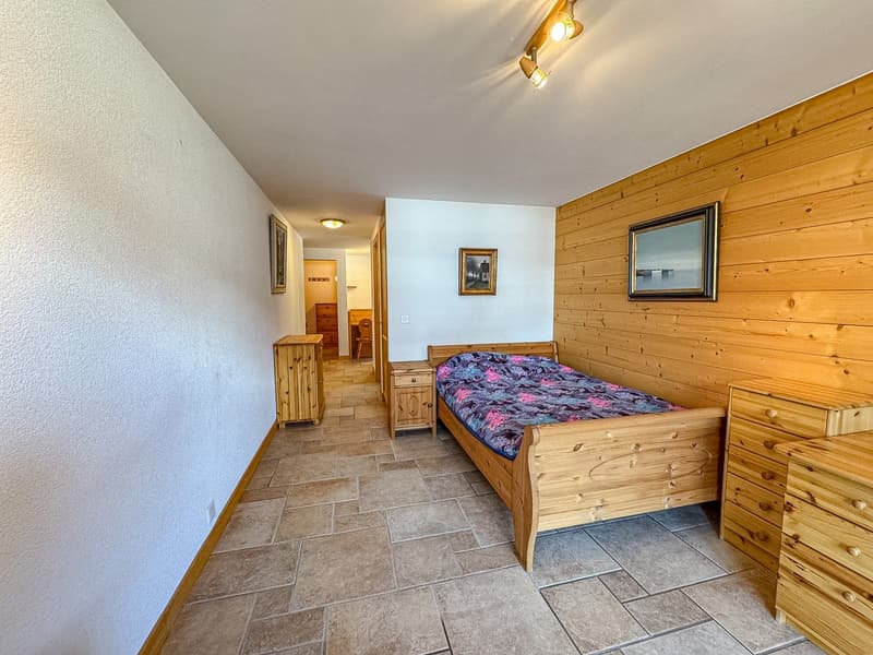 Bedroom with wooden bed, wooden nightstands, wooden dressers, wooden walls, tiled floor, picture frames, ceiling lights, power outlet.