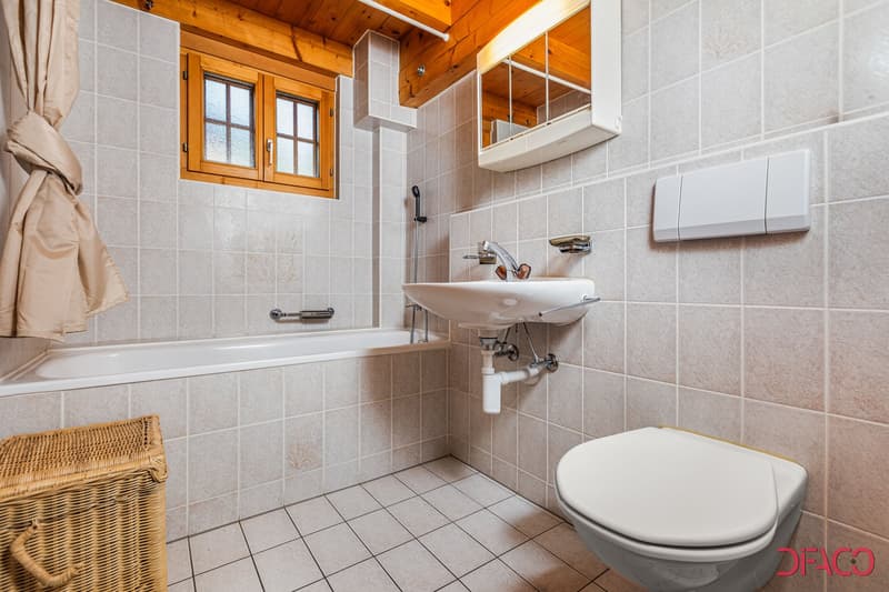 Tiled bathroom with wooden ceiling, large window, sink, toilet, and storage cabinet