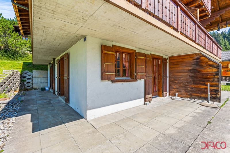 Exterior of a chalet-style building with stone walls and wooden balconies. It features a row of wooden doors and windows.
