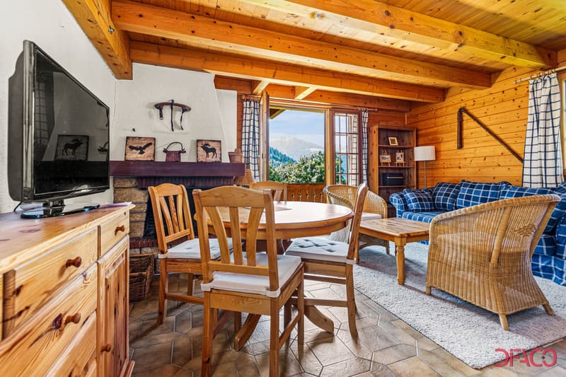 living room with wooden walls, a wooden fireplace, wooden furniture, round table and chairs, couch with blue plaid covers, TV on a dresser, rug, side table, lamps