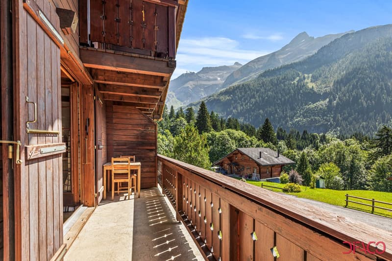 Wooden mountain cabin with a balcony/terrace overlooking a scenic mountain landscape with forests and peaks in the background