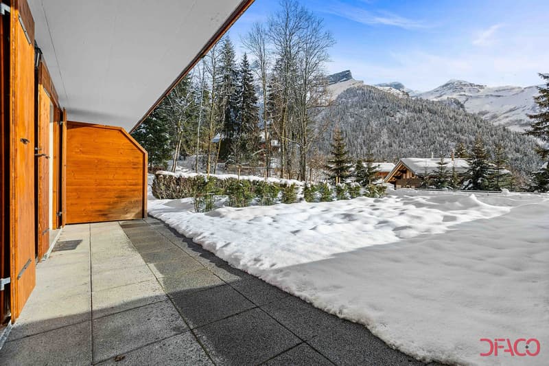 Wooden cabin-style house with a covered porch, surrounded by snow-covered trees and mountains in the background