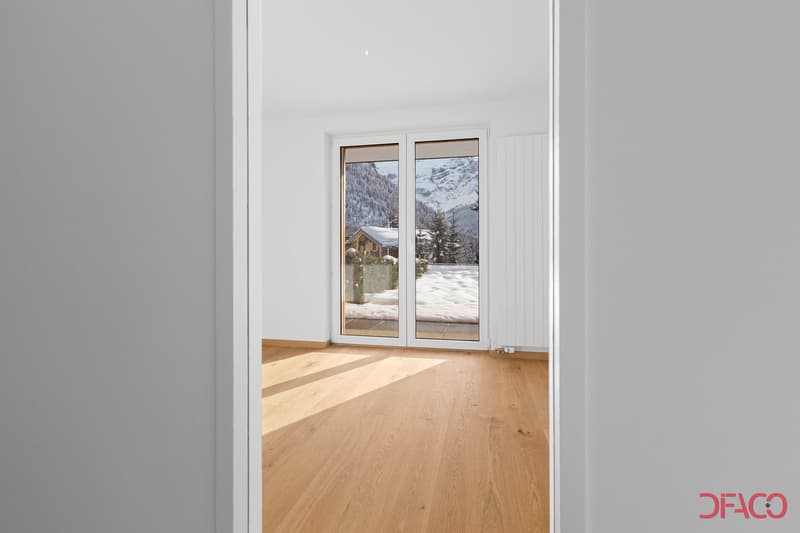 Spacious room with large windows overlooking a snowy mountain landscape, hardwood flooring, and white walls.