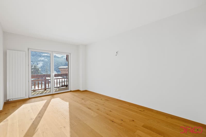 Spacious room with large windows overlooking a snowy mountain landscape, hardwood flooring, and a balcony or terrace accessible through the windows.