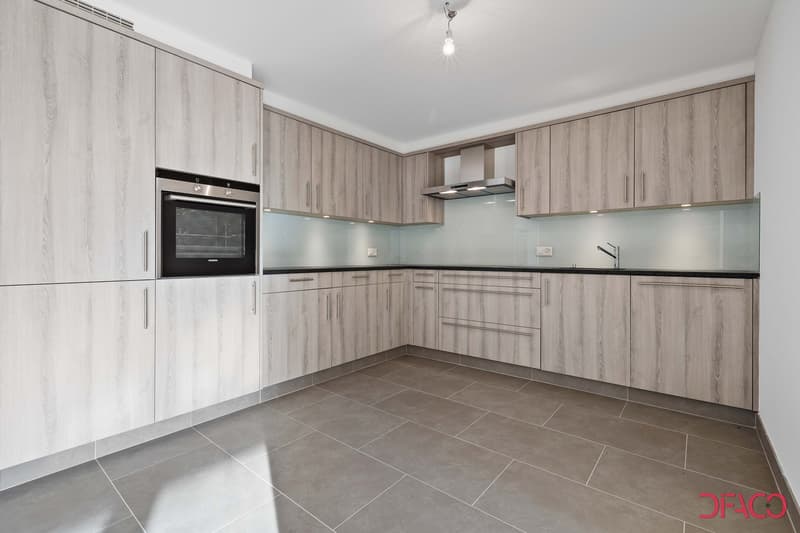Spacious modern kitchen with gray wood-paneled cabinets, built-in oven, and gray tile flooring
