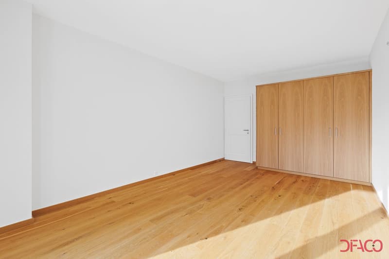Spacious bedroom with white walls, wooden flooring, and a large built-in wardrobe along one wall.
