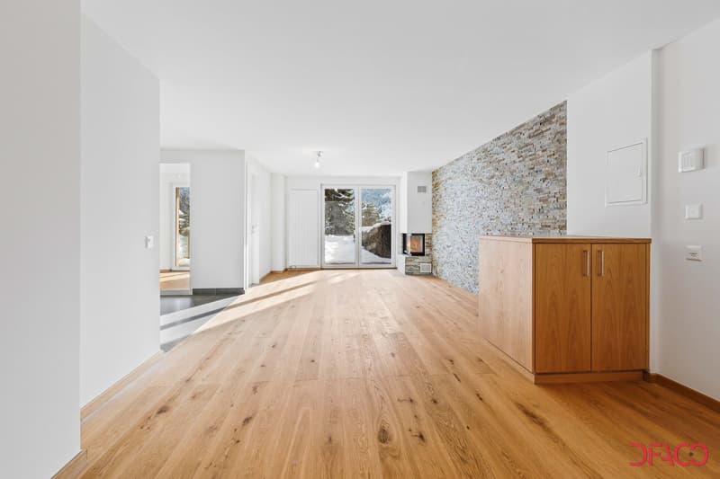 Spacious open-plan living area with hardwood floors, white walls, large windows, a stone fireplace, and built-in wooden cabinets