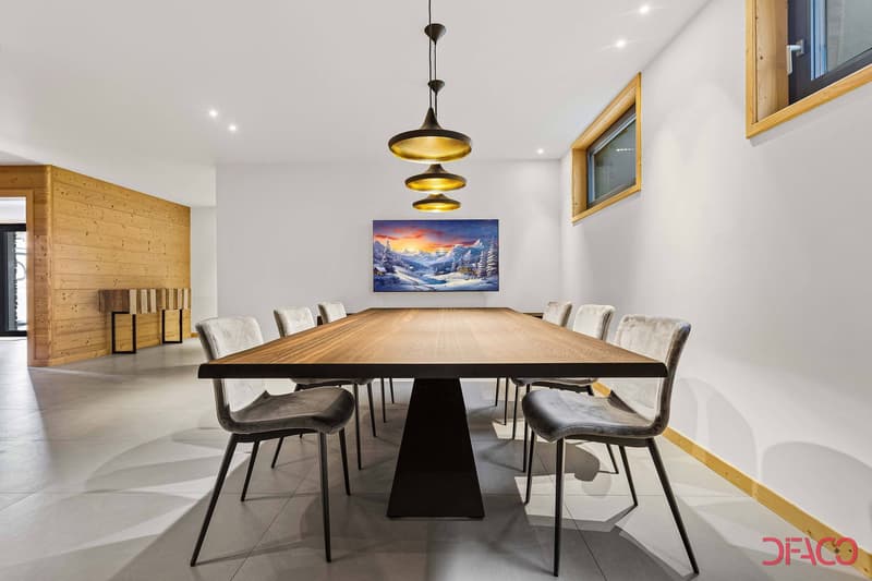 Large wooden dining table with black chairs, pendant lighting fixture, wooden wall paneling, large landscape painting on the wall