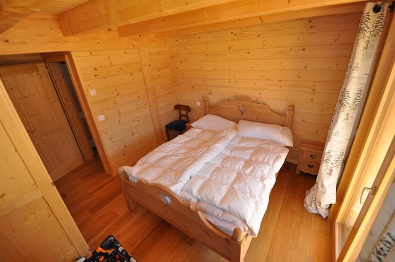 Cozy wooden bedroom with a rustic wooden bed, wooden walls and ceiling, and a fireplace visible in the room.
