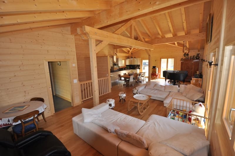 Spacious open-concept living area with wooden beamed ceiling, large windows, comfortable sofas, dining table, and a fireplace