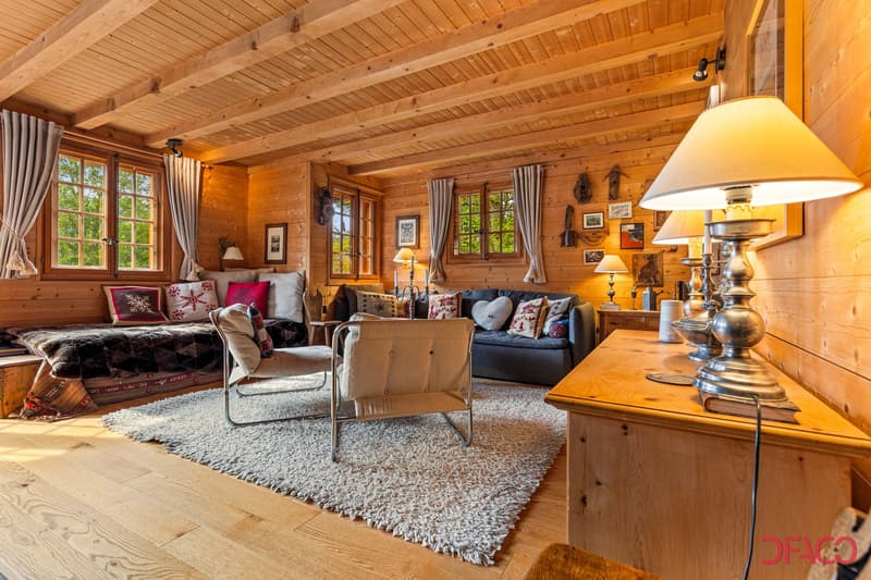 Cozy log cabin living room with wooden walls and ceiling, large windows, plush sofas and chairs, area rug, and decorative lamps and accessories