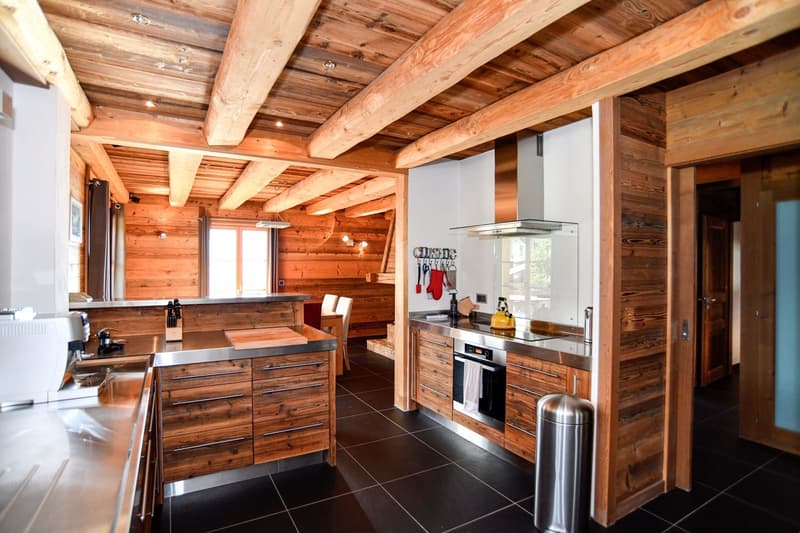 Rustic kitchen with wooden beams and paneling, stainless steel appliances, wooden cabinets and drawers, tile flooring