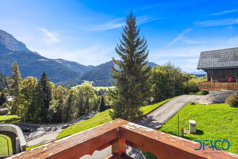 balcony with wooden railing, surrounded by trees, mountains in the background