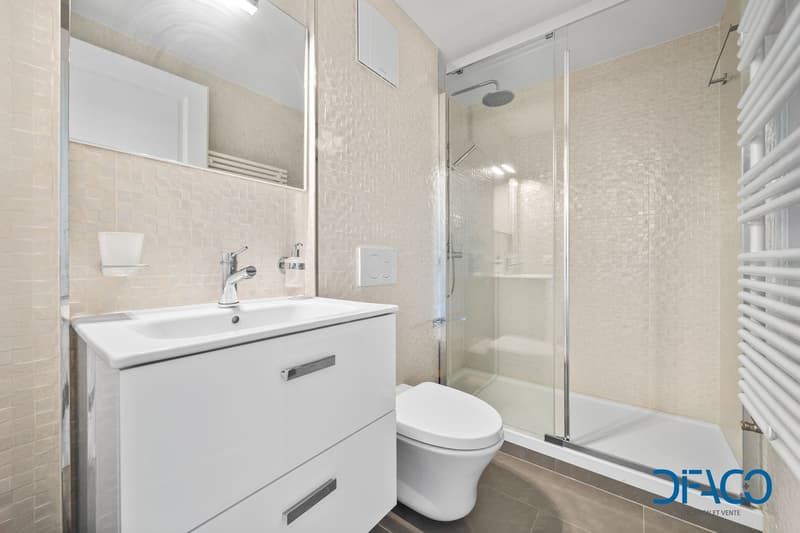 Modern bathroom, glass walk-in shower, white toilet, white vanity with double drawers, tiled walls, wall-mounted radiator, overhead lighting