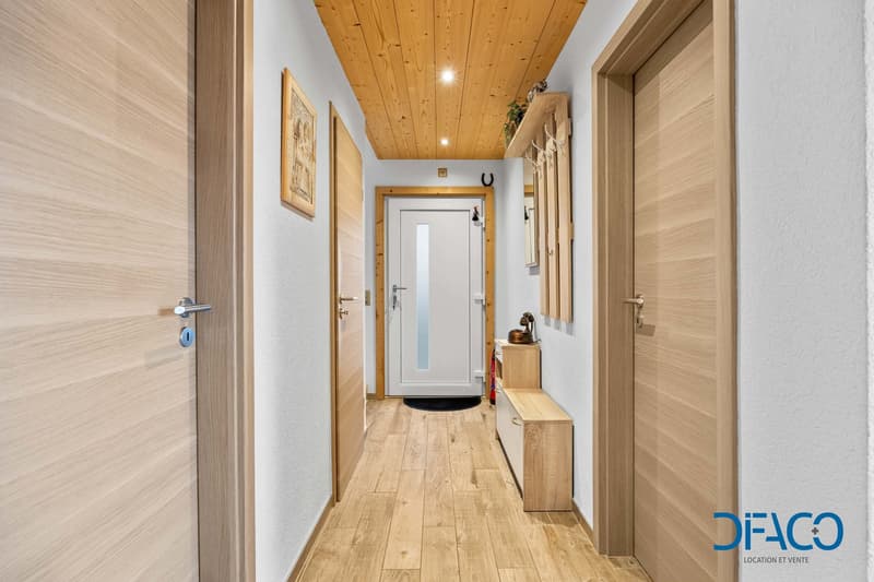 Wooden floor, wooden doors, white walls, wooden ceiling, open door, shoe rack, hanging plant, fire extinguisher, mirror, black mat.