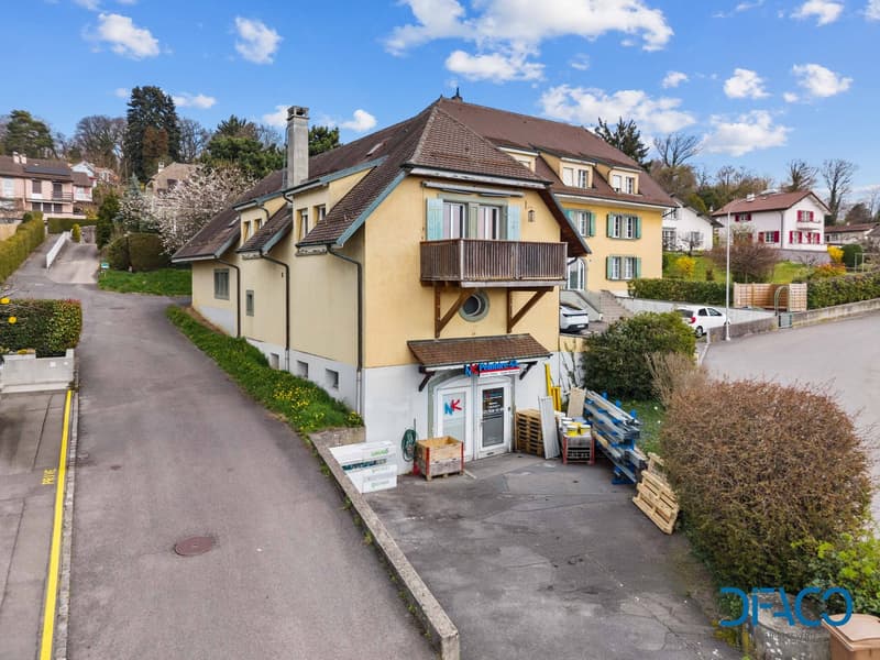 2 story house, yellow exterior, brown roof, balcony, driveway, parked cars, greenery