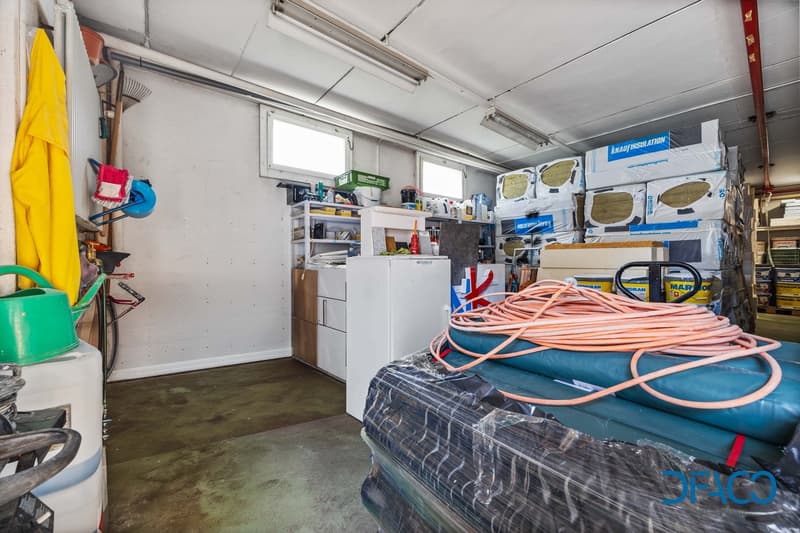 Storage room with white walls, ceiling lights, shelves, storage boxes, tools, and a white refrigerator.