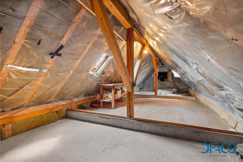 unfinished attic with wooden beams, plastic sheeting, wooden table, storage boxes, windows