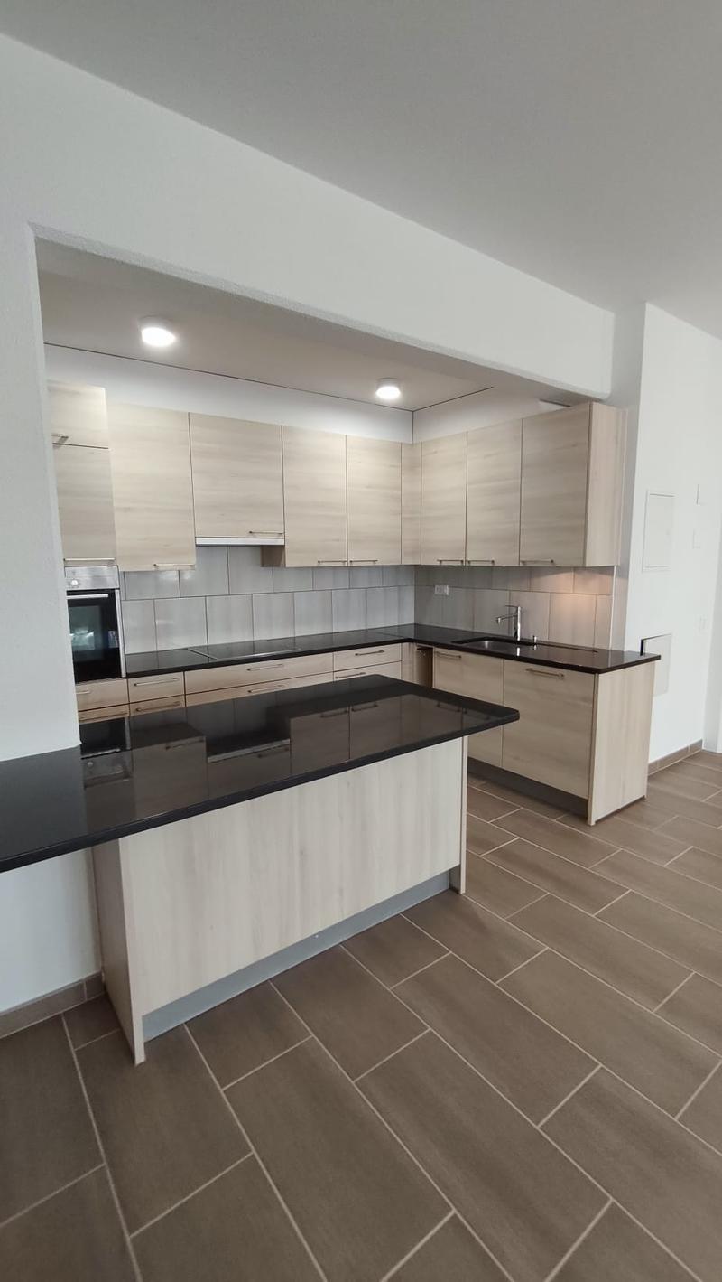 modern kitchen with island, black countertops, wooden cabinets, built-in oven, dishwasher, washing machine