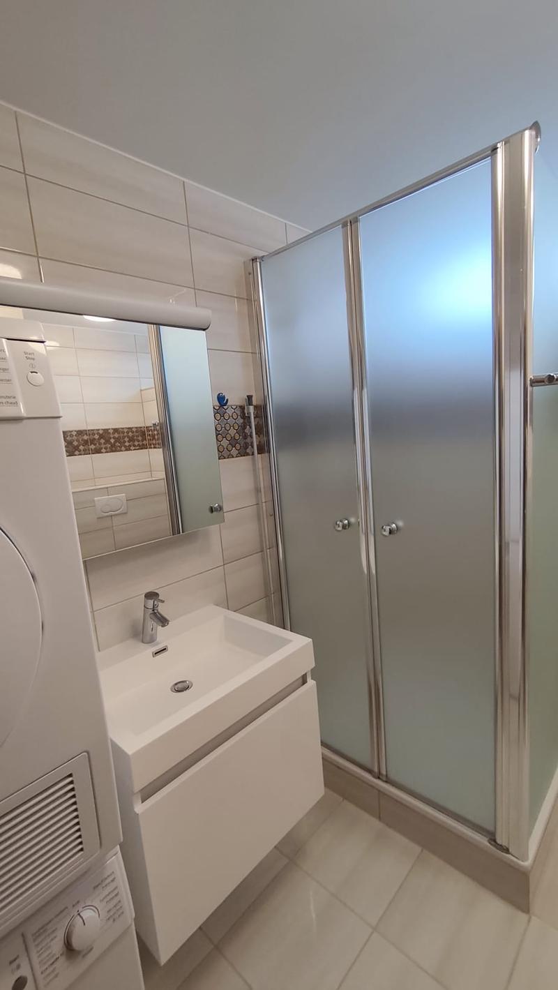 Bathroom with white tiles, white sink, mirror, washing machine, shower enclosure