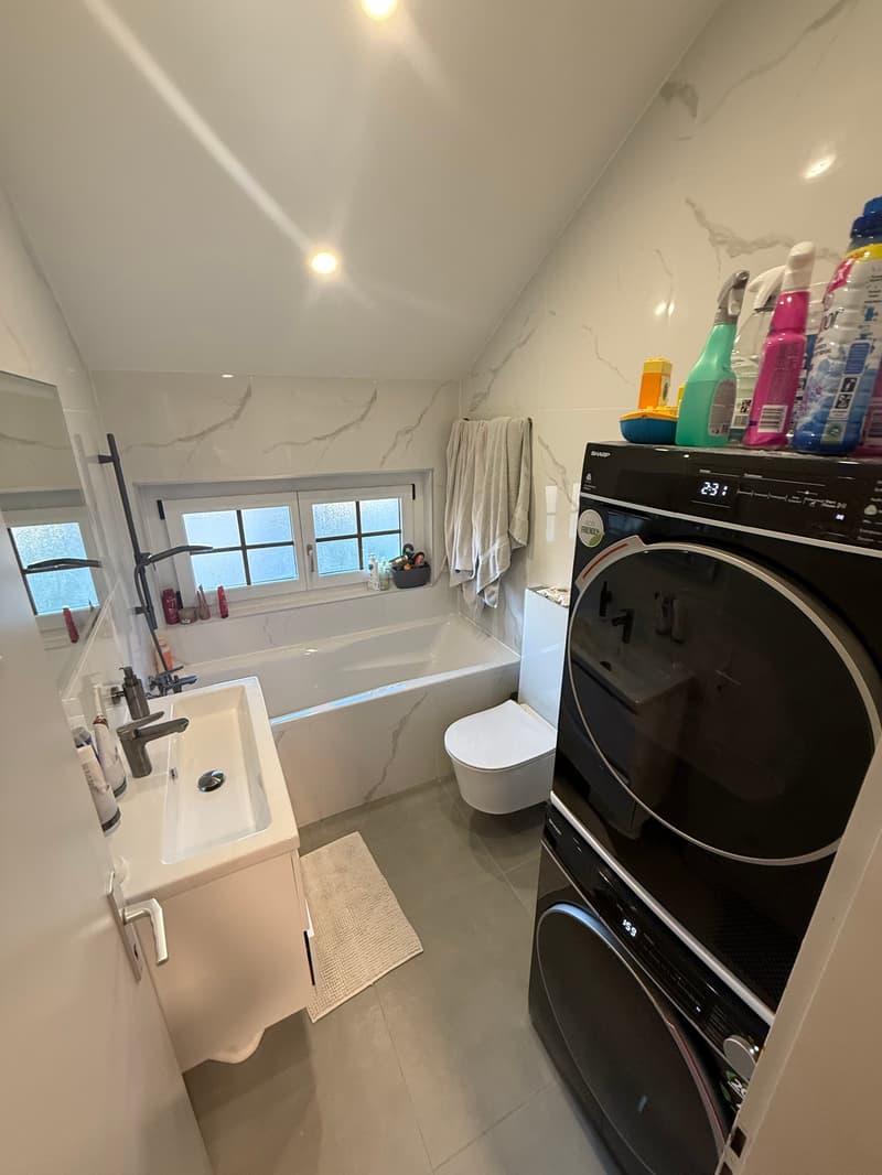 Bathroom with bathtub, sink, toilet, tiled walls and floor, washer, and dryer.