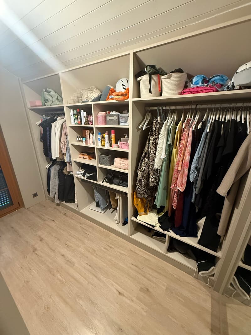 Large, well-organized closet with numerous shelves and hanging space for clothes and accessories, wood floor