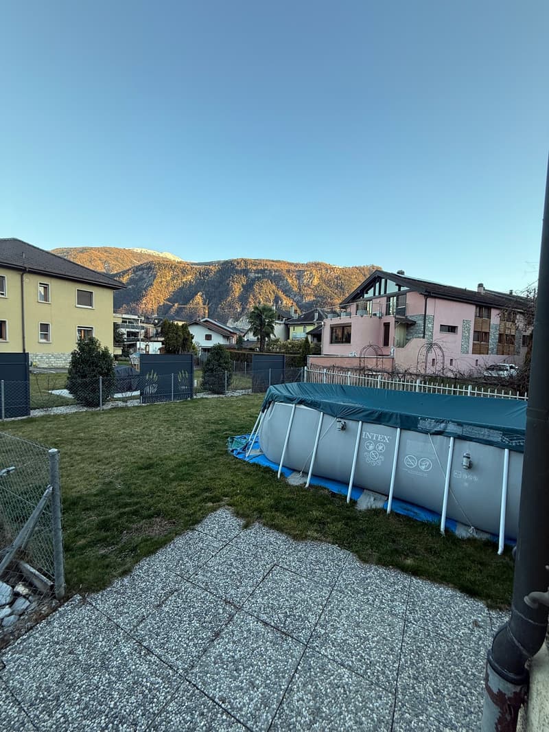 well-maintained garden with a large swimming pool, gravel pathway, green lawn, several fences, mountains in the distance