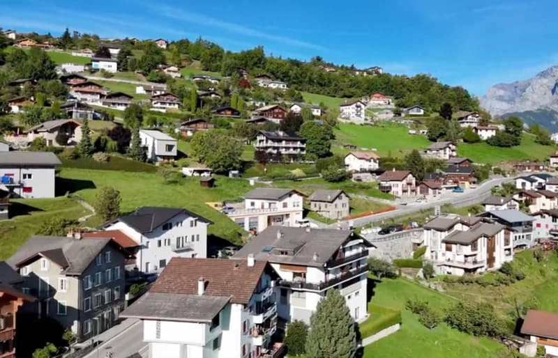 Mountainside village with many houses, green surroundings, mountainous terrain, roads and pathways