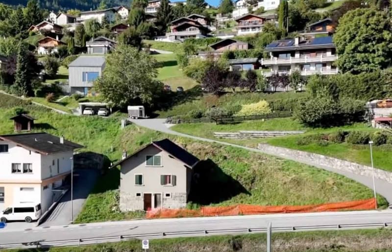 hilltop residential area, multiple houses, paved road, greenery, parked vehicles, road barriers