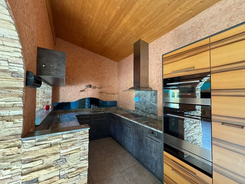 modern kitchen with granite countertops, wooden cabinets, stainless steel appliances, stone wall, wooden ceiling