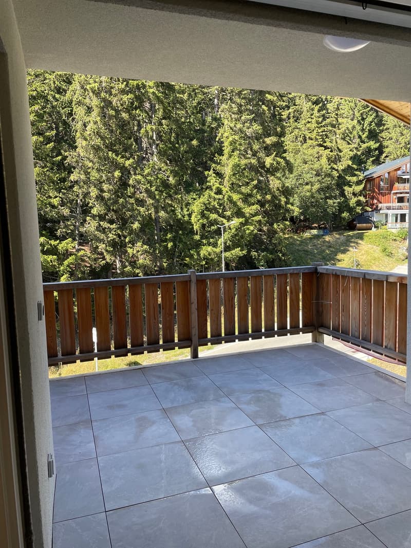 Tiled floor balcony with wooden railings, street lamp visible, open balcony door, surrounding trees and grass