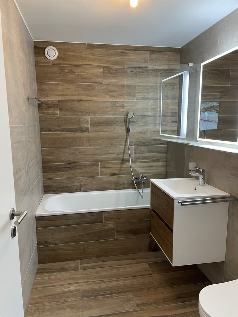 Bathroom with bathtub, wooden flooring, wooden shower cabin, wall mounted sink, mirror, toilet