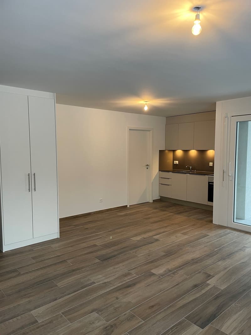 large empty room, wooden floor, white kitchen, electrical outlets, entrance door, sliding door, cabinets