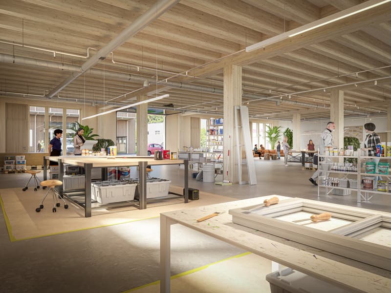An open space with multiple workstations, tables, chairs, shelves with products, and people. The floor is carpeted, and the ceiling is wooden beams with exposed metal pipes and white fluorescent lighting.