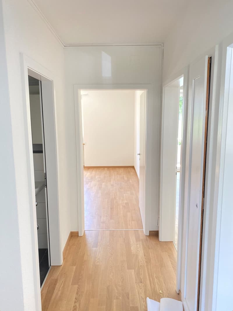 empty corridor with hardwood floors, white walls, two doors on the right side leading to a room and an open door to the left side