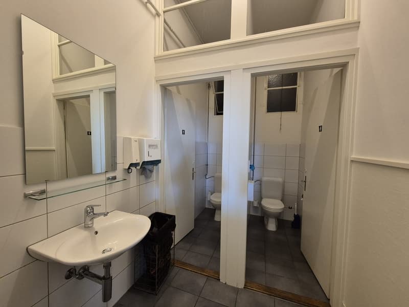 modern bathroom with toilet, sink, mirror, trash can, and paper towel dispenser