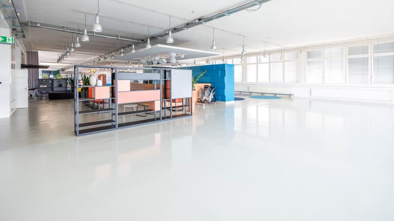 Spacious office with suspended lamps, white floor, white walls, several glass windows, various office furniture and accessories