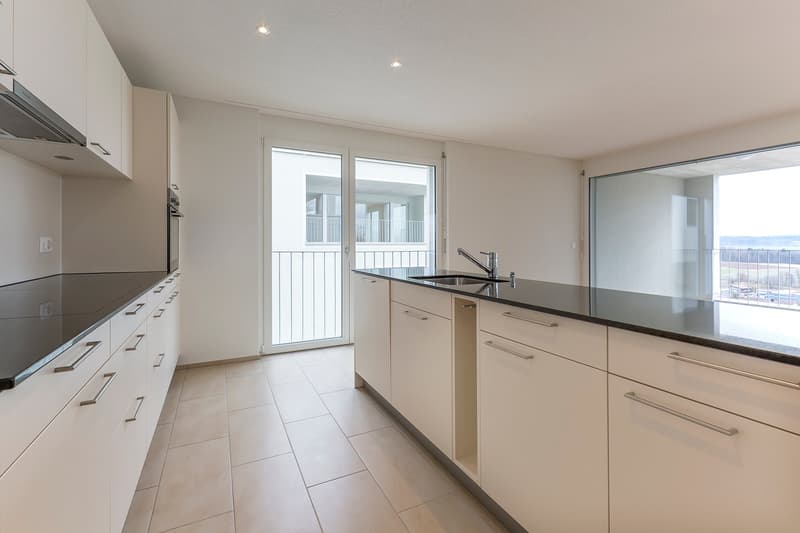modern kitchen with white cabinets, black countertops, stainless steel sink, glass door leading to balcony