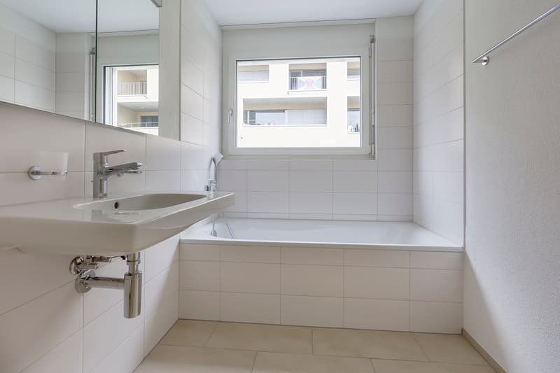 Bathroom with white tiles, bathtub, sink, mirror, and shower head