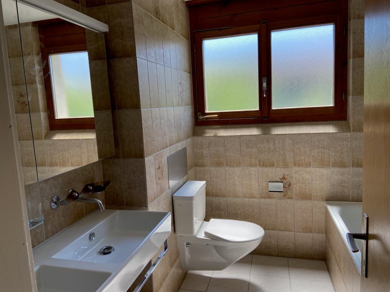 Bathroom with white sink, white toilet, bathtub, and tiled walls and floor.