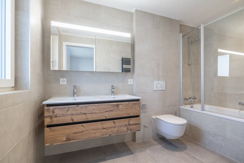 modern bathroom with double sink, wooden cabinet, glass shower enclosure, bathtub, and toilet