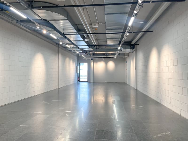 Empty room with white walls, gray floor, ceiling lights, and an open door.