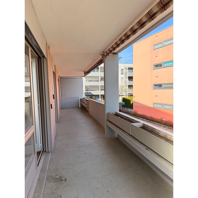 Balcony with concrete floor, glass doors, metal railing, planter boxes, and a view of a building.