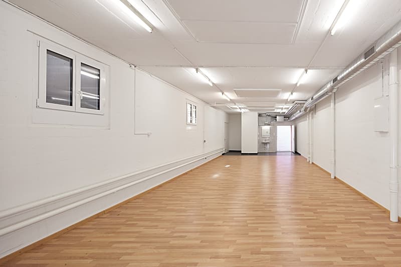 Empty room with white walls, wooden floor, windows, and ceiling lights