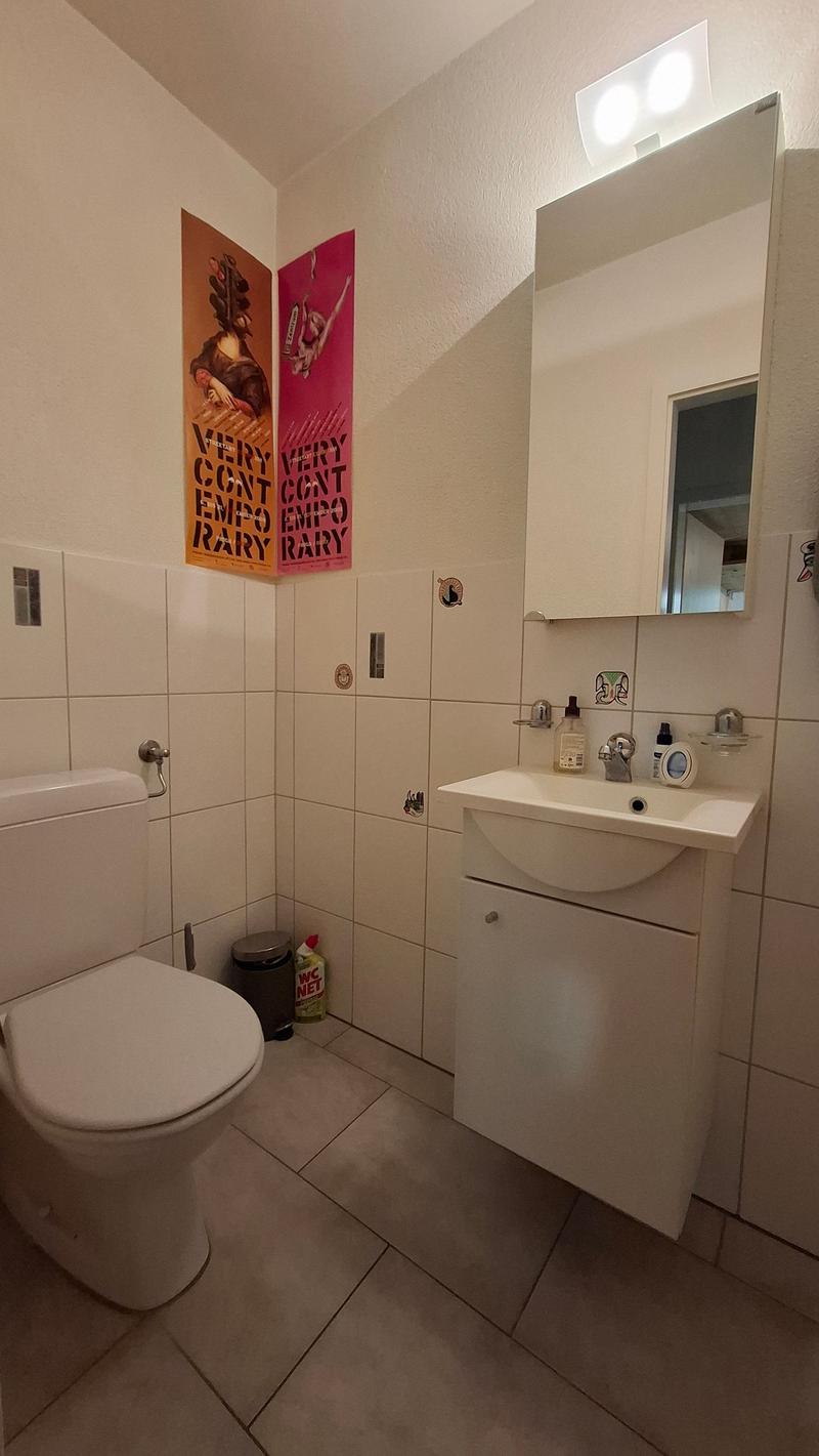 Bathroom with white tiles, white toilet, white sink, mirror, and posters on the wall