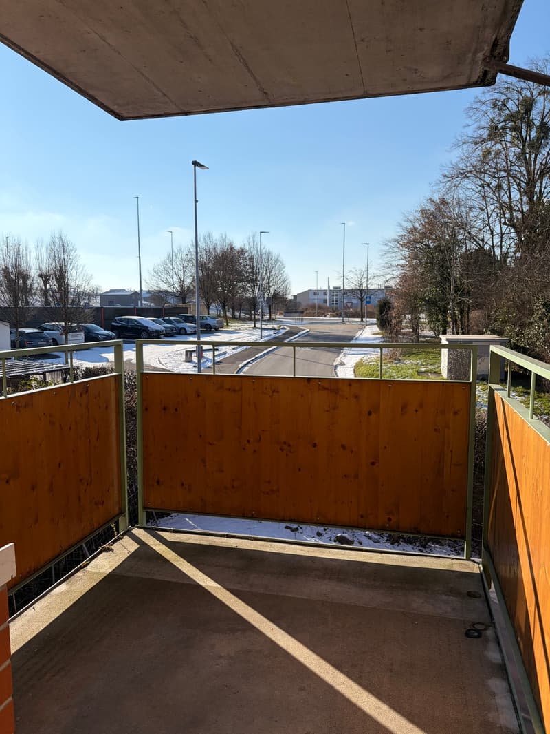 Balcony with wooden railings, view of a parking lot and road, snow on the ground, trees, street lights