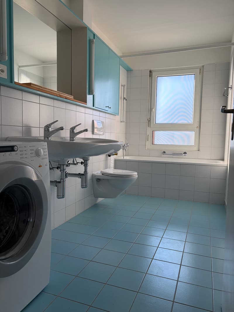 Bathroom with blue tiles, white sink, toilet, bathtub, washing machine, mirror, and window
