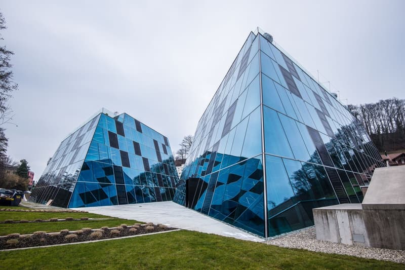Two modern, angular glass buildings with a blue and gray geometric design. The buildings have a unique, pyramidal shape and are surrounded by a grassy area with landscaping.