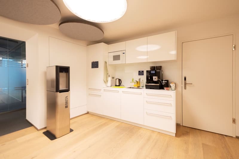 Modern, white kitchen with built-in appliances including a dishwasher and washing machine, hardwood flooring, and recessed lighting fixtures.